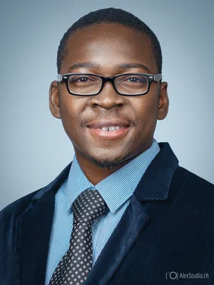 Confident photo for a resume or CV featuring a smiling professional in glasses, patterned tie, striped shirt, and dark jacket against light blue.