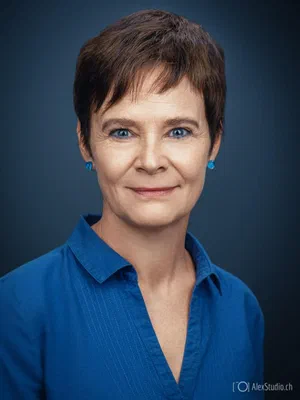 Approachable business portrait with a composed smile, vivid blue blouse, matching earrings, and flattering studio light on a deep blue background.