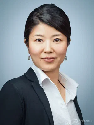 Elegant photo for business showing a poised professional in a black blazer and crisp white shirt, evenly lit against a soft blue background.
