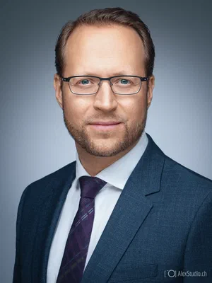 Refined executive portrait of a calm professional in glasses, textured blue suit, white shirt, and purple tie, by Alex, Photographer based in Geneva, Switzerland.
