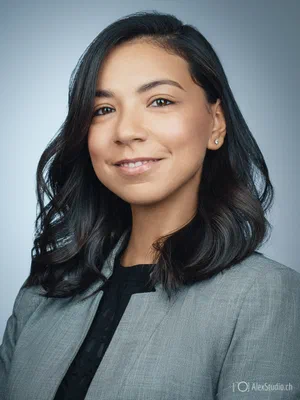 Modern LinkedIn profile photo with a relaxed smile, softly waved hair, grey blazer, and black top against a clean blue-grey studio background.