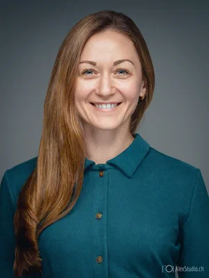 Natural photo for business featuring a warm smile, long auburn hair, and a teal collared top, softly illuminated against a neutral grey background.