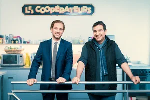 Lively corporate photo of two smiling men in contrasting formal and casual attire, leaning together on a railing in a colorful workplace.