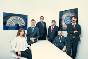 Contemporary corporate group portrait of six people arranged around a white conference table, framed by colorful geometric artwork and clean architecture.
