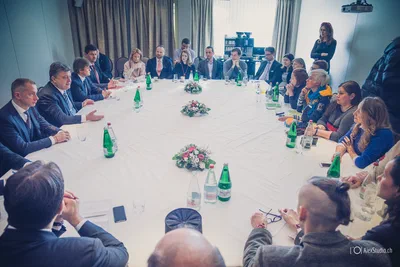 Delegates gather around a long white table for a formal discussion, with attentive expressions and balanced corporate photography framing the entire room.