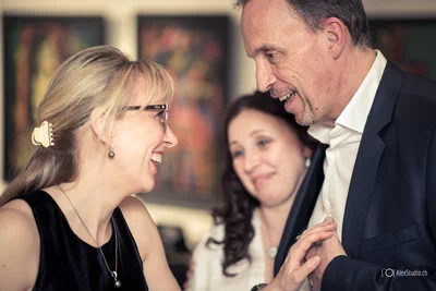 Two guests laugh warmly during a reception as another attendee looks on, preserving an expressive, spontaneous moment of corporate event photography.