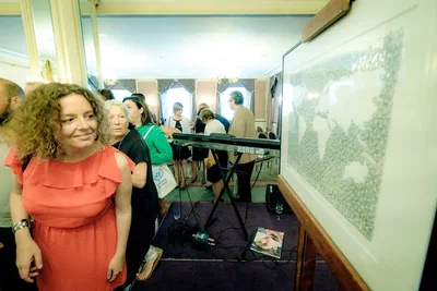 Guests gather around an interactive screen while a woman in a coral dress studies the display, captured in lively documentary event photography.