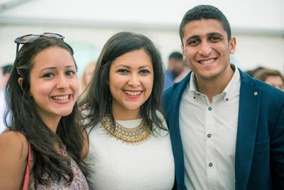 Three young guests pose shoulder to shoulder with bright smiles, creating a friendly, polished group portrait during a social reception.