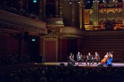 A chamber ensemble performs beneath an ornate pipe organ as a seated audience watches, captured in atmospheric event photography within a grand concert hall.