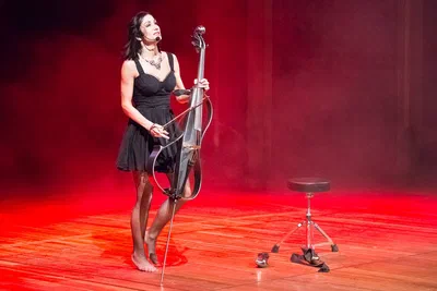 A barefoot musician performs with an electric cello under dramatic red stage lighting, an expressive event image by Alex, a Geneva-based photographer.