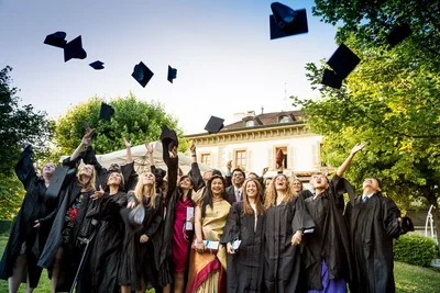 Graduates joyfully toss their mortarboards into the air outside a stately building, creating a spirited event photograph filled with celebration.