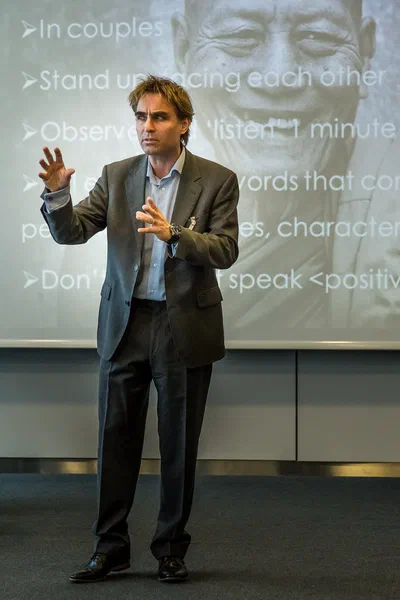 A suited presenter gestures expressively before a projected workshop slide, creating a focused portrait of communication and audience engagement.