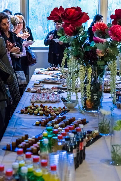 Guests gather beside an abundant reception buffet, where vivid red flowers, miniature desserts, and refreshments create an elegant sense of occasion.