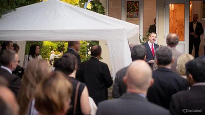 An outdoor speaker addresses a formally dressed audience beneath a white canopy, captured in polished corporate event photography by Alex, photographer from Geneva, Switzerland.