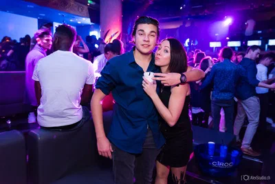 Two guests pose playfully together amid a busy dance floor, framed by saturated purple lighting and the lively atmosphere of the event.