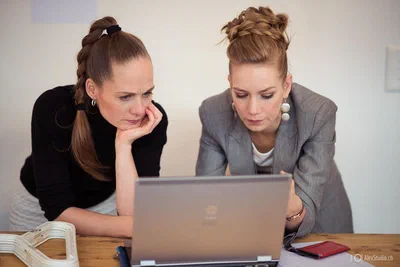 Two women lean over a laptop with concentrated expressions, a candid moment of collaboration captured through attentive corporate photography.