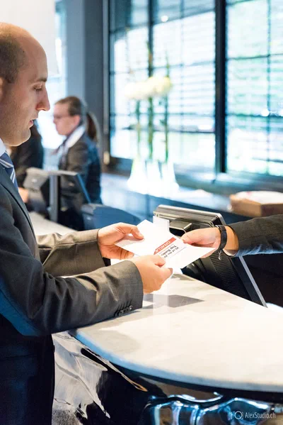 A suited guest receives printed materials across a marble reception counter, illustrating the professional welcome and organization of a corporate event.