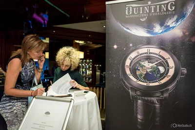 Two attendees review documents at a high table beside a dramatic watch display, blending candid interaction with refined brand-event photography.