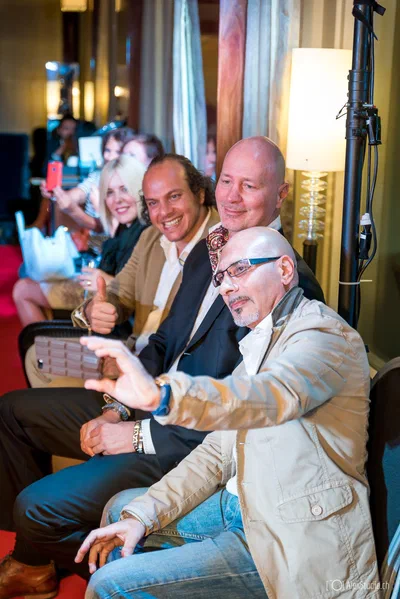 Seated guests lean together for a cheerful smartphone selfie, capturing the sociable, spontaneous character of an evening gathering.