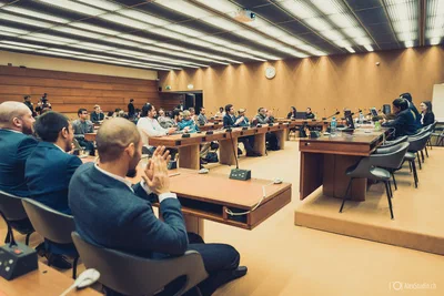 Delegates applaud across a modern auditorium arranged with microphones and tiered desks, captured through wide-angle conference photography in Geneva.