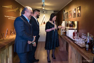Guests observe a guided tasting among neatly arranged bottles and glasses, a warm candid scene from brand-event photography by Alex, photographer from Geneva, Switzerland.
