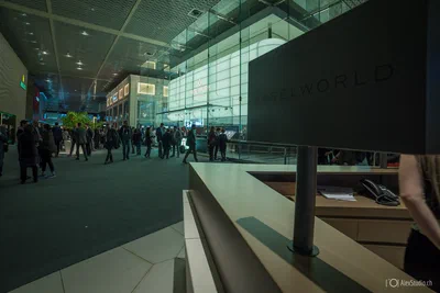 Visitors circulate through a spacious contemporary exhibition hall beside a prominent BASELWORLD desk, establishing the scale and atmosphere of the trade event.