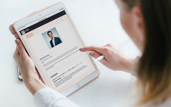 A person browses an online publication on a tablet, featuring a suited man's headshot above article text and an orange-accented layout.