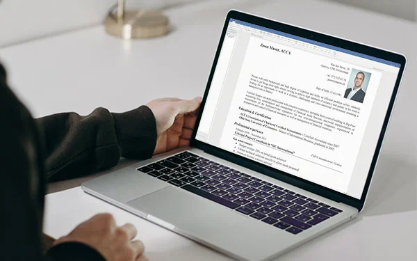 A person reviews a résumé on a laptop, where a polished photo for a CV appears beside professional text and contact details.