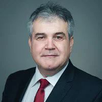 A gray-haired man in a dark suit and red tie faces the camera for a classic photo for résumé or CV.