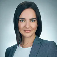 A woman with a sleek dark bob wears a gray blazer and white top in a confident business photo against pale gray.