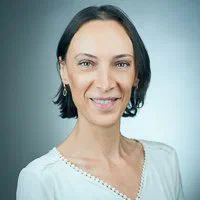 A woman with short dark hair smiles in a white beaded-neckline top for a softly lit professional headshot by Alex in Geneva.